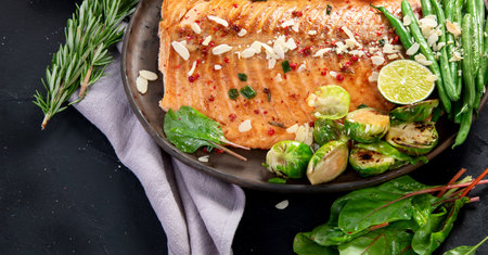 Cooked salmon with fresh vegetables, lime and souce. Baked fish on dark background. Top viewの写真素材