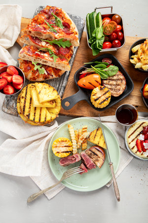Table with grilled food. Pizza, corn, tomatoes, peppers, cooked meat. BBQ time. Top viewの写真素材