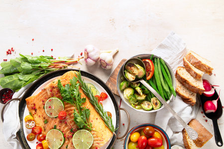 Grilled salmon and vegetables on wooden light background. Dinner table with cooked fish, tomatoes, asparagus. Top view, copy spaceの写真素材