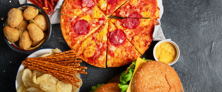 Large table of assorted take out food such as pizza, French fries, onion rings, burgers and snacks on a dark background. Top view. Panorama with copy space.の写真素材