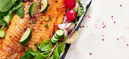 Cooked salmon with fresh greens and lime. Baked redfish on light wooden background. Top view,...