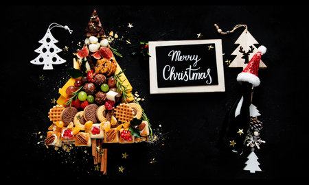 Christmas tree with sweets and cookies decoration on dark background. Holiday food. Top view.