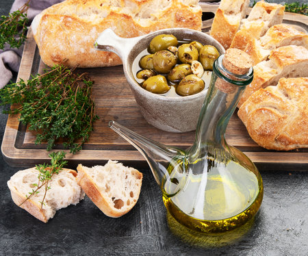 Fresh bread with olive oil and olives on dark gray background. Top view, copy spaceの写真素材