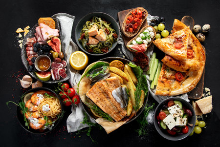 Assortment of various Mediterranean food - fish, seafood, sauces, pasta, snacks, pizza on a black background. Top view.の写真素材
