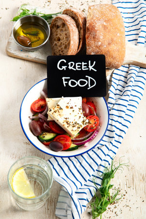 Fresh vegetable healthy Mediterranean food salad of Greek feta cheese, onion, tomato, olives, cucumber and bread on board. Top view, light background.の写真素材