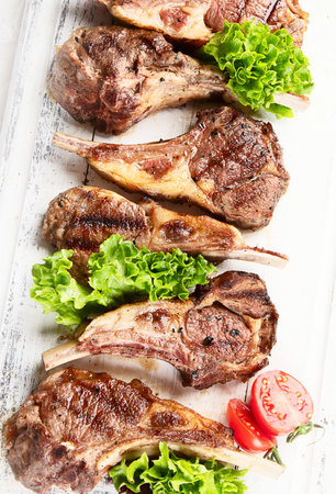 Grilled lamb ribs with tomatoes and salad. Rack of lamb chop on white wooden board. Top viewの写真素材