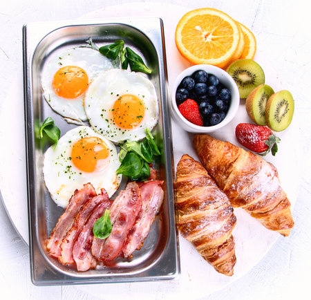 Table set for traditional breakfast with eggs, bacon, croissants and berries on a white background.. Top viewの写真素材