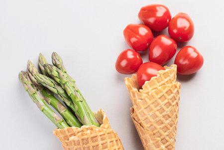 Healthy vegetables in waffle cones, asparagus and tomatoes on a gray background. Vegan and vegetarian diet concept. Top view.の写真素材