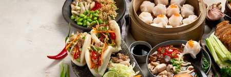 Set of Chinese dishes on dark background: sweet duck, soup, steamed buns, dim sum in bamboo steamer, salad, rice, dips. Asian style banquet, top view. Panorama with copy space.の写真素材