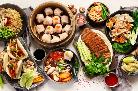 Set of Chinese dishes on dark background: sweet duck, soup, steamed buns, dim sum in bamboo steamer, salad, rice, dips. Asian style banquet, top view.の写真素材