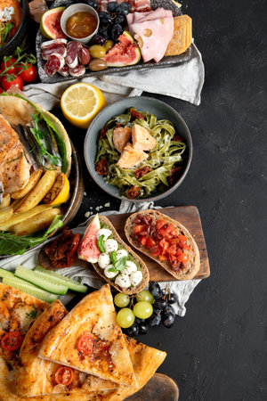 Assortment of various Mediterranean food - fish, seafood, sauces, pasta, snacks, pizza on a black background. Top view. Copy space.の写真素材