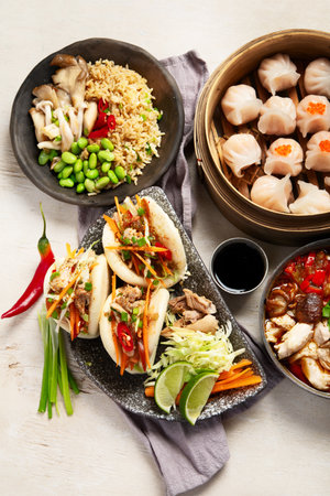Set of Chinese dishes on dark background: sweet duck, soup, steamed buns, dim sum in bamboo steamer, salad, rice, dips. Asian style banquet, top view.の写真素材