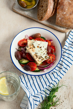 Fresh vegetable healthy Mediterranean food salad of Greek feta cheese, onion, tomato, olives, cucumber and bread on board. Top view, light background.の写真素材