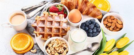 Breakfast table with eggs, berries, yogurt, waffle and croissant. Spring breakfast. Top view. Panorama.の写真素材