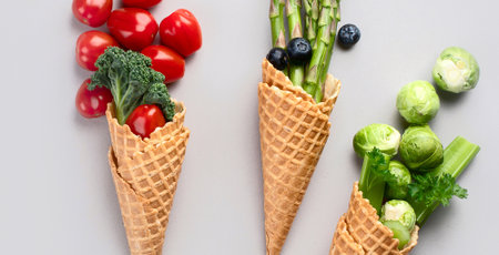 Healthy fresh egetables in waffle cones, asparagus, tomatoes, Brussels sprouts on a gray background....