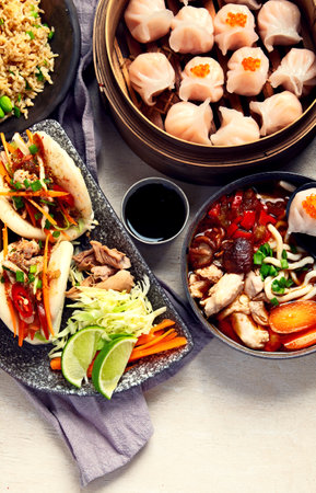 Set of Chinese dishes on dark background: sweet duck, soup, steamed buns, dim sum in bamboo steamer, salad, rice, dips. Asian style banquet, top view. Copy space.の写真素材