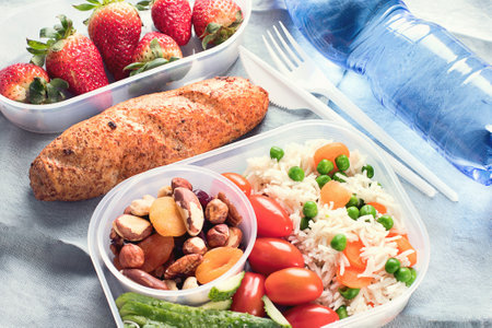 Healthy lunch boxes with rice, vegetables, fruits, nuts and bottle of water on a gray background. Top view.の写真素材