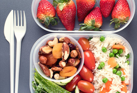 Healthy lunch boxes with rice, vegetables, fruits, nuts and bottle of water on a gray background. Top view.の写真素材