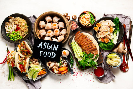 Set of Chinese dishes on dark background: sweet duck, soup, steamed buns, dim sum in bamboo steamer, salad, rice, dips. Asian style banquet, top view.の写真素材