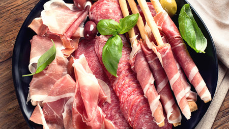 Plate with prosciutto, salami, bread sticks and olives on a wooden background. Top viewの写真素材