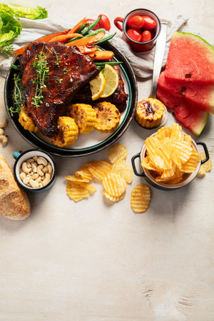 BBQ ribs with vegetables, sauce, roasted corn and watermelon on a white background. Top view. Copy space.の写真素材