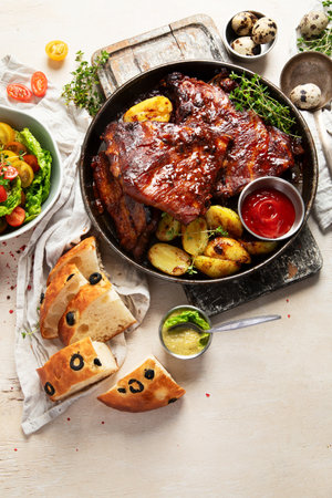 Tasty roasted ribs with baked potatoes vegetables and olives on a white background. Top view. Copy space.の写真素材