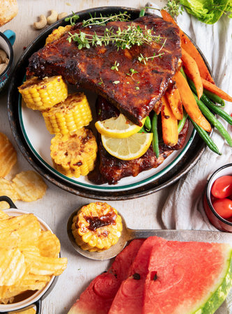 BBQ ribs with vegetables, sauce, roasted corn and watermelon on a white background. Top view.の写真素材