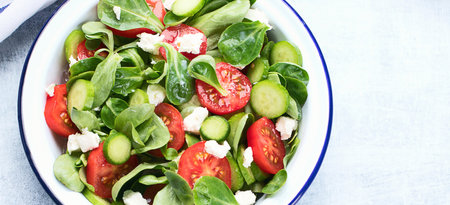 Fresh vegetable salad with feta cheese in a plate on a blue background. Traditional Greek salad. Top view. Panorama with copy space.の写真素材