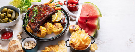 BBQ ribs with vegetables, sauce, roasted corn and watermelon on a white background. Top view. Panorama with copy space.の写真素材