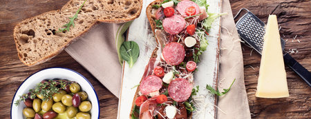 Sandwich with ciabatta, prosciutto, cheese and lettuce with olives on a wooden background. Top view. Panorama.の写真素材