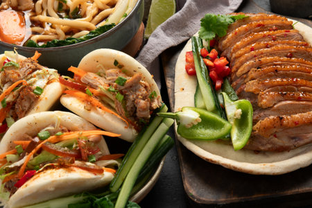 Set of Chinese dishes on dark background: sweet and sour duck, noodles soup, steamed buns. Asian style banquet or buffet, top view.の写真素材