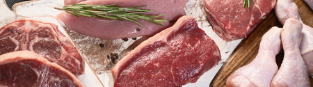 Different types of raw meat - beef, pork, lamb, chicken on dark background. Top view. Panorama.