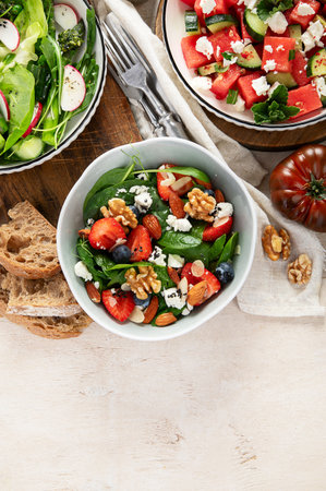 Various summer salads with strawberry, herbs. Healthy salad with arugula, peaches, burrata, blueberries and walnuts on a light background. Top view, copy space.の写真素材