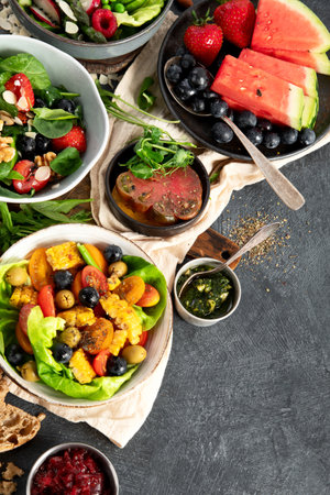 Fresh vegan summer salads with vegetables, fruits and nuts on a dark background. Top view. Copy space.の写真素材