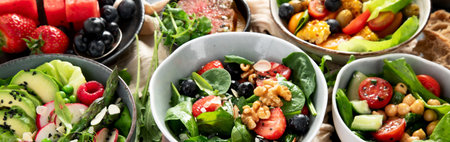 Fresh vegan summer salads with vegetables, fruits and nuts on a dark background. Top view. Panorama.の写真素材