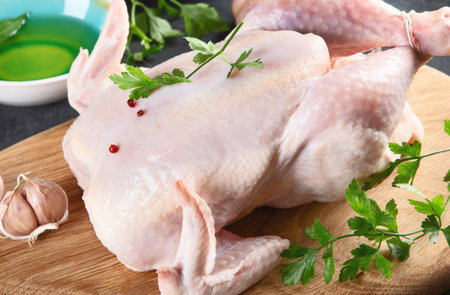 Whole chicken with seasonings on wooden cutting boardの写真素材