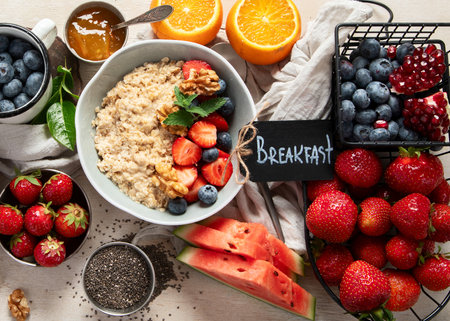 Organic ingredients for healthy breakfast - yoghurt, nuts, fresh fruits, oatmeal, whole grain flakes on white background. Top view.の写真素材