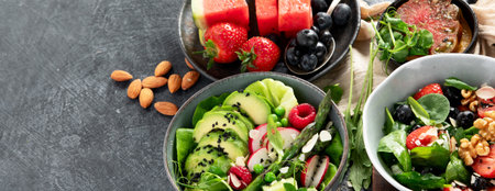 Fresh vegan summer salads with vegetables, fruits and nuts on a dark background. Top view. Panorama...