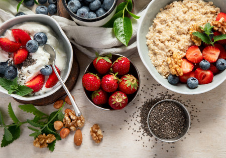 Organic ingredients for healthy breakfast - yoghurt, nuts, fresh fruits, oatmeal, whole grain flakes on white background. Top view.の写真素材