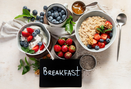 Organic ingredients for healthy breakfast - yoghurt, nuts, fresh fruits, oatmeal, whole grain flakes on white background. Top view.の写真素材