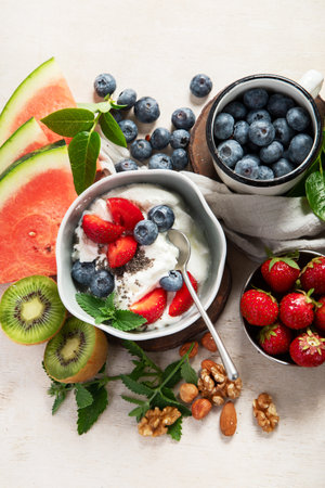 Organic ingredients for healthy breakfast - yoghurt, nuts, fresh fruits, oatmeal, whole grain flakes on white background. Top view.の写真素材