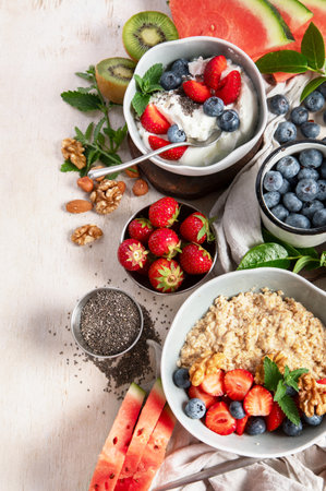 Organic ingredients for healthy breakfast - yoghurt, nuts, fresh fruits, oatmeal, whole grain flakes on white background. Top view. Copy space.の写真素材