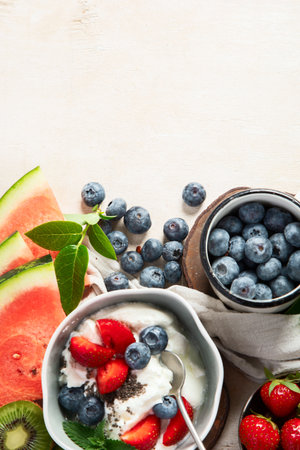 Organic ingredients for healthy breakfast - yoghurt, nuts, fresh fruits, oatmeal, whole grain flakes on white background. Top view. Copy space.の写真素材