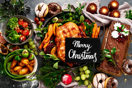 Christmas dinner with roast chicken, potato, cake and snacks on a black background. Top view.