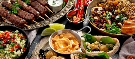 Middle Eastern or Arabic cuisine with a variety of dishes on a dark background. Top view. Panorama.