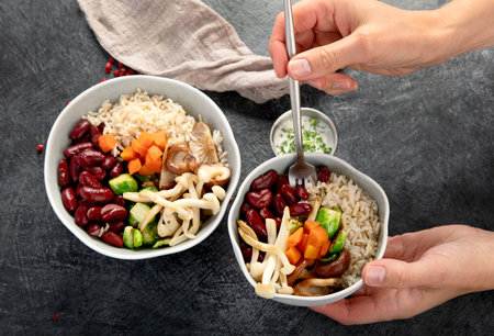 Cooked white rice mixed with colorful vegetables (mushroom, carrots, red beans) in bowls on a dark...