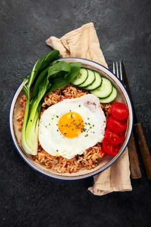 A plate of Nasi Goreng with rice, vegetables, and an egg on top on a dark background. Top view.の写真素材