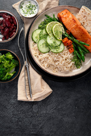 Fried salmon fish fillets with rice, vegetables and lime on a plate on a dark background. Top view.の写真素材