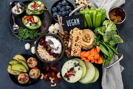 Various hummus dips. Hummus plate with vegetable snacks. Carrot, celery sticks. Vegan and traditional hummus as healthy and vegan snack on a dark background. Top view.の写真素材