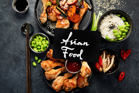 Set of assorted chicken dishes on table: sweet and sour chicken on plate, chicken legs with chilli sauce on a dark background. Top view.の写真素材